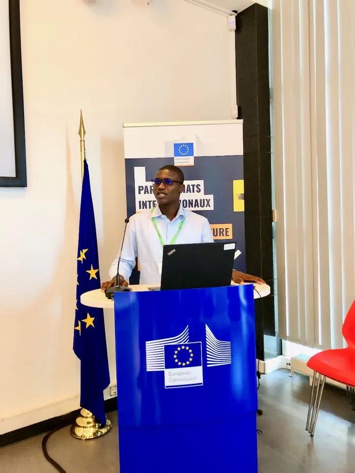 Konoutan Medard Kafoutchoni speaking at a European Commission lectern, EU flag to his left