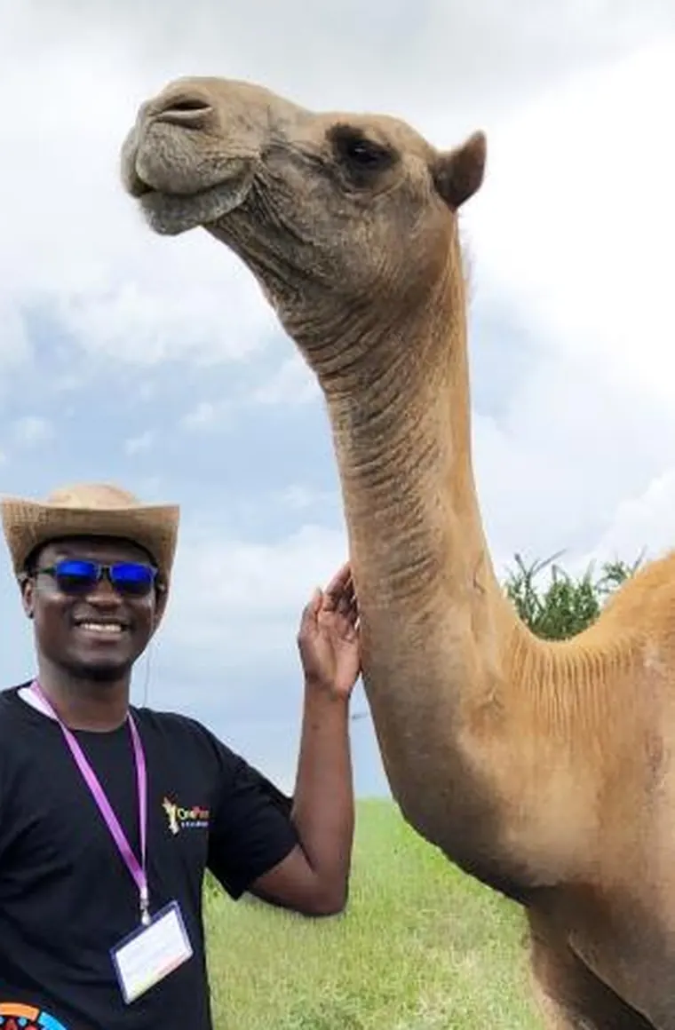 Konoutan Medard Kafoutchoni in Kenya, One Planet Fellowship badge around his neck, beside a camel